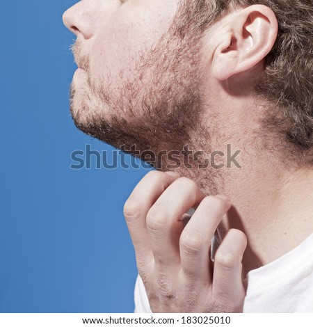 A man scratches his beard with hand against a blue background.
