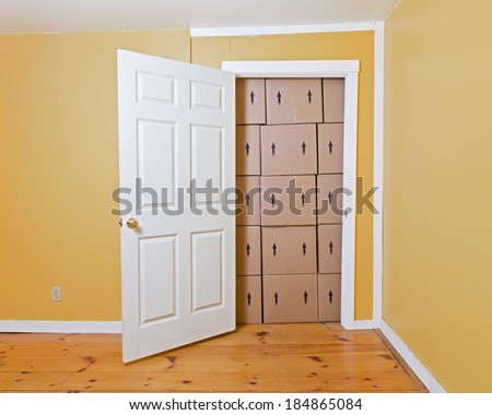 A white door opens in a yellow room to reveal a room full of brown cardboard boxes.