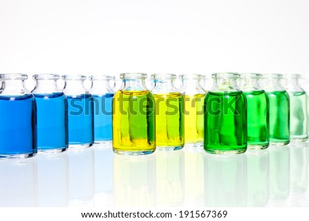 Colorful Science Vials. Several vials on a glass table top with different tones of green, yellow and blue.
