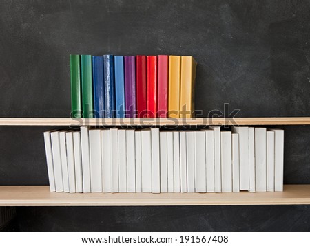 Books and Blackboard. A row of multi-colored books sits on the top shelf above a row of all white books in front of a chalkboard.