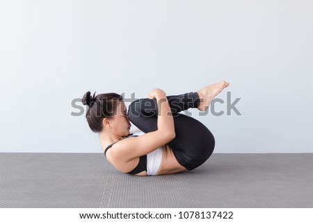 Beautiful young woman wearing sportswear practicing yoga in studio,natural light.Pavanamuktasana (Wind-Relieving Pose).Concept : yoga poses for beginner. #1078137422