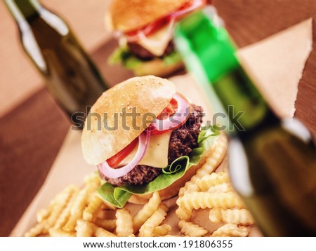Beer bottles and burgers in the background. Focus is on the burger
