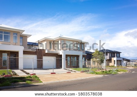 Brand new residential townhouses behind temporary construction fences in an Australian suburb. Concept of real estate development, house for sale and housing market. Melbourne, VIC Australia.