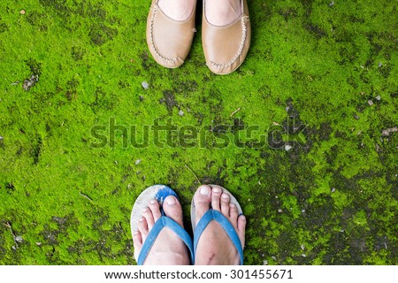 Male foot in flip-flop and female foot in a brown leather shoes on grass
