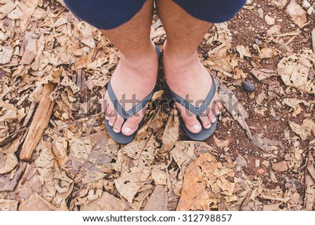 Male foot in flip-flop on dry leaf
