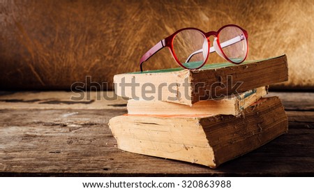 still life of old books and eyeglasses on wooden floor with brown leather background