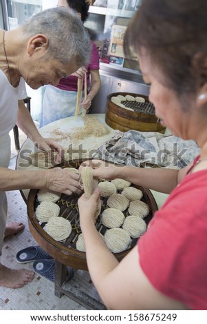 MACAU, CHINA - 26 SEPTEMBER 2013 - A family prepares thin handmade Macau style noodles in a streetside kitchen in the old town, on 26 Sept 2013, in Macau, China.