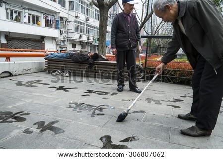 SHANGHAI, CHINA - 17 MARCH 2013 - Men take turns to write Chinese characters with water on the ground in a park by Suzhou Creek, Shanghai