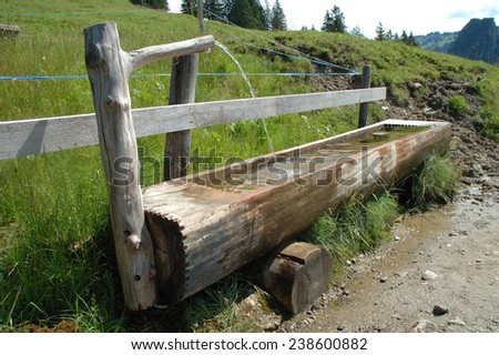 Old wooden trough filled with water standing at wooden fence.