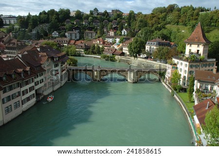 Bern, Switzerland - August 15, 2014: Bridge (Untertorbrucke), buildings and trees at Aare river in Bern, Switzerland. Unidentified people visible.