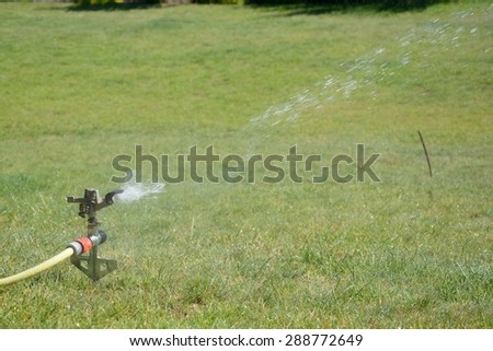 Sprinkler splashing with water on lawn in garden
