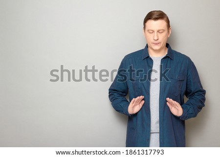 Studio shot of man wearing shirt, with eyes closed, relaxing, meditating, making breath exercises, relieving stress, trying to concentrate and calm down, standing over gray background, with copy space ストックフォト © 