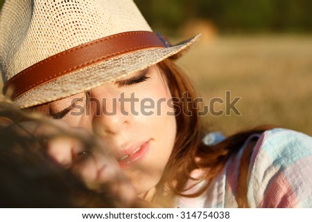 Portrait of resting young girl in a hat on field with hay bales in sunny summer day