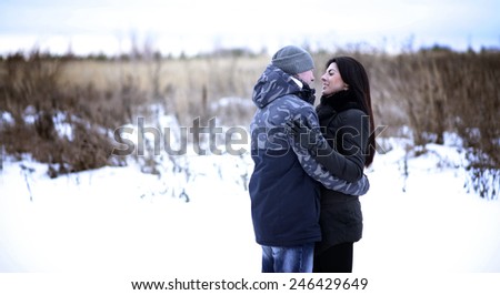 Happy young couple hugging outdoors in a snowy park. Love hugs, family relationships.