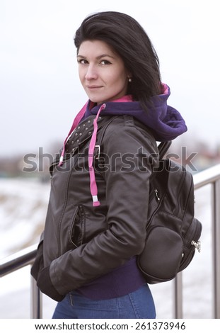 Outdoors beautiful young brunette woman posing in a black leather jacket with Fashionable Leather backpack