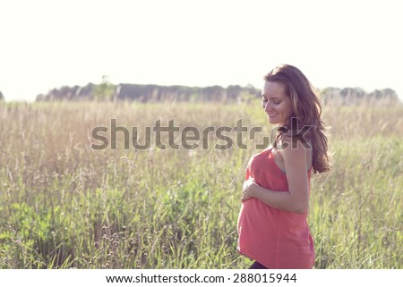 Bright sunny young mother hugging her belly and think about your baby, on the summer meadow
