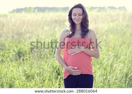 Fashionable pregnant woman standing in a field in the summer dreaming of the future child