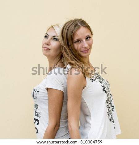 Two girlfriends, beautiful young blonde brunette fashion style of urban life, in the white shirt on the background wall, summer day, smiling, enjoying a rest