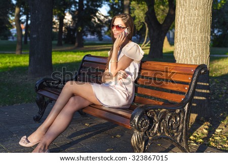 Beautiful emotional brunette girl laughing on the phone in the park summer glasses pink dress, enjoy your holiday in the city. Fashion style of life, a bright summer day.