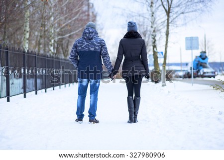 Couple holding each other\'s hands, the winter goes on the road, enjoying a stroll, a love couple. Fashion lifestyle. Husband and wife are going through the park holding hands in the winter.