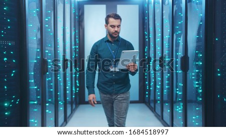 Caucasian IT engineer activating digital database server room with tablet. Bearded specialist inspecting rack internet servers at data center computer security. Zoom out.