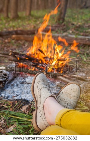 Recreation scene: woman feet in light brogues by camp fire in spring forest