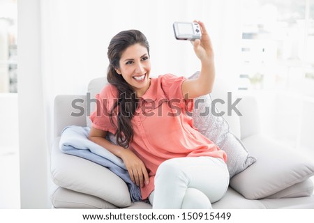 Pretty brunette sitting on her sofa taking a picture of herself at home in the sitting room