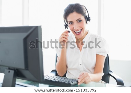 Happy call center agent sitting at her desk on a call in her office