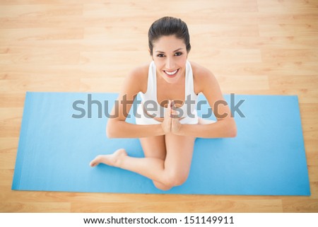 Fit woman sitting in cow face pose smiling at camera at home on wooden floor