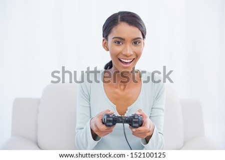 Smiling woman sitting on sofa in bright living room playing video games