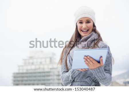 Cheerful woman with winter clothes on using her tablet outdoors on a cold grey day