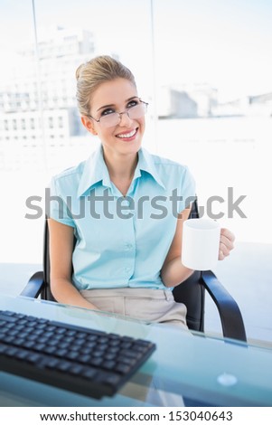 Smiling businesswoman wearing glasses holding coffee in bright office