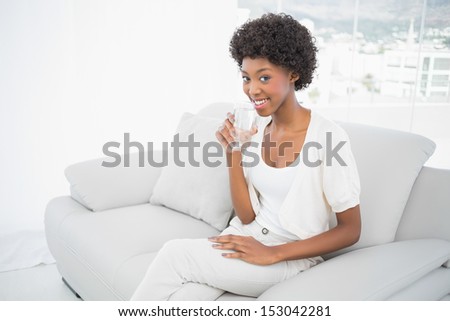 Happy gorgeous brunette drinking water sitting on cosy sofa