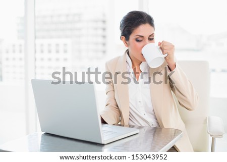 Cheerful businesswoman drinking from mug while working on laptop at the office
