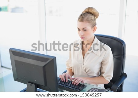 Stern young blonde businesswoman looking at her computer at office