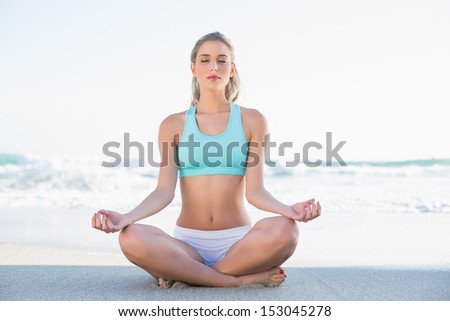 Relaxed slender blonde in sportswear meditating on a sunny beach
