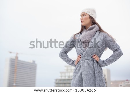 Unsmiling pretty brunette with winter clothes on posing outdoors on a cold grey day