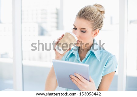 Peaceful classy woman using tablet while drinking coffee in bright office