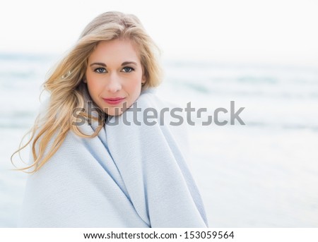 Thoughtful blonde woman covering herself in a blanket on the beach