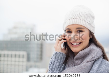 Smiling brunette with winter clothes on having a call outdoors on a cold grey day