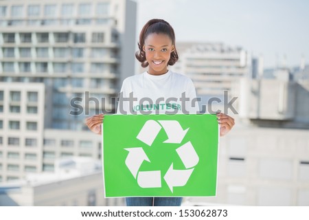 Cheerful woman holding recycling sign outdoors on urban background