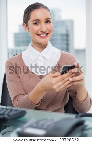 Cheerful beautiful businesswoman in bright office text messaging