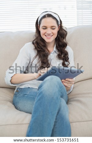 Smiling casual woman on cosy couch in bright living room using tablet pc