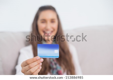 Happy young model in bright living room holding her credit card