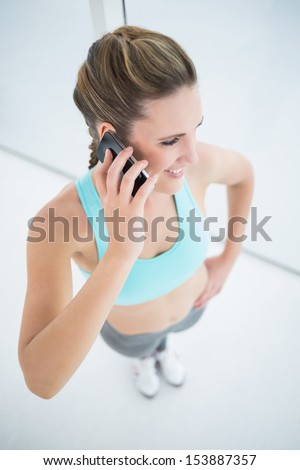Fit woman in sportswear talking on mobile phone in bright fitness studio