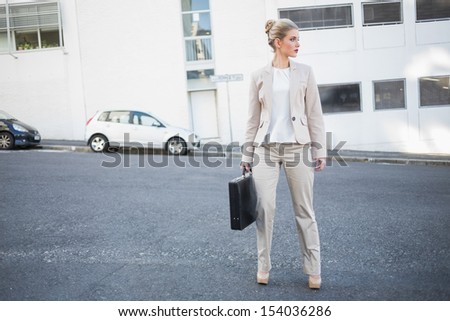 Serious classy businesswoman holding briefcase posing outside on urban background