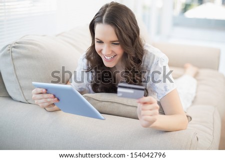 Smiling woman lying on a cosy couch buying online with her credit card