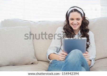Casual woman on cosy couch in bright living room using tablet pc