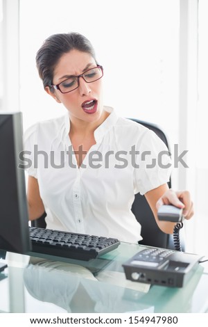 Angry businesswoman sitting at her desk hanging up the phone in her office