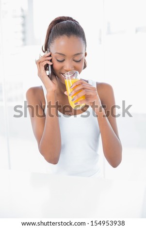 Happy athletic woman phoning while drinking orange juice in bright fitness studio